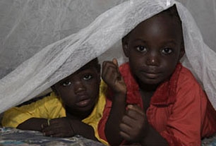Two children peek from under a bed net in the Garki area of A...